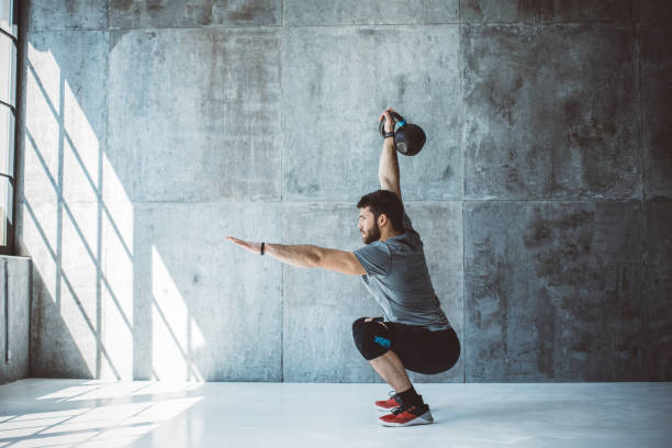 Male fitness athlete performing overhead squat with kettlebell